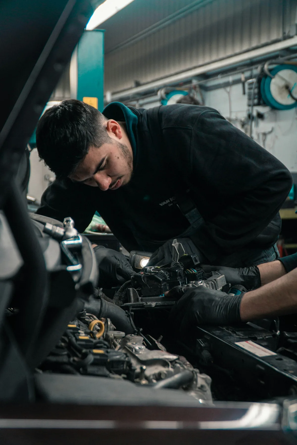 A mechanic working in a car engine bay checking the alternator and drive belt